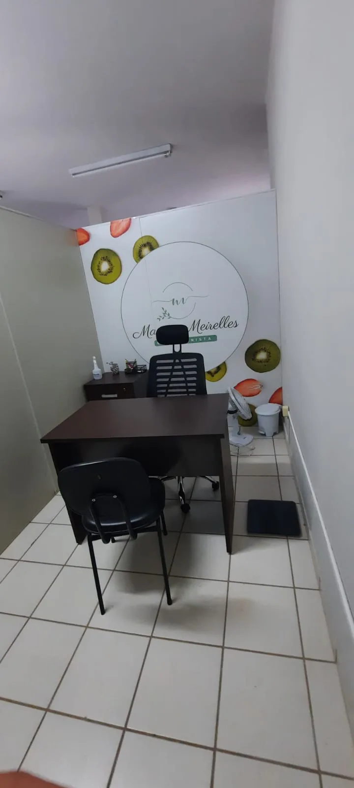 Consultório com mesa, cadeiras e a parede decorada com o logo da Marina Meirelles e fatias de frutas